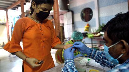 Un sanitario toma una muestra de sangre a una joven para detectar malaria y dengue en Mumbai.