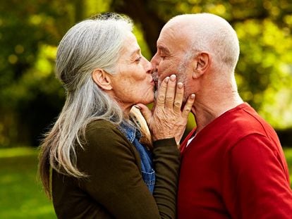 Una pareja de mayores se besa en un parque.