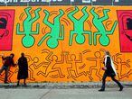 NEW YORK - MAY 02:  People walk by a re-creation of an untitled mural painted by artist Keith Haring on the corner of Houston Street and Bowery in Manhattan May 2, 2008 in New York City. Marking the 50th anniversary of Haring's birth on May 4, a team of artists recreated the mural which was originally done in 1982 as Haring's first major outdoor project. The original mural only existed for a few months before the Day-Glo colors began to decompose in the sun and Haring painted over the piece.  (Photo by Mario Tama/Getty Images)