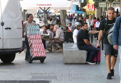 A delivery person parks on the sidewalk of Atocha street to leave merchandise;  in the background, terraces of various premises. 