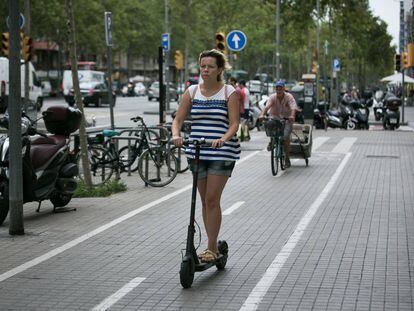 Una mujer circula con un patinete eléctrico por el carril bici de la acera de la Gran Via de Barcelona.