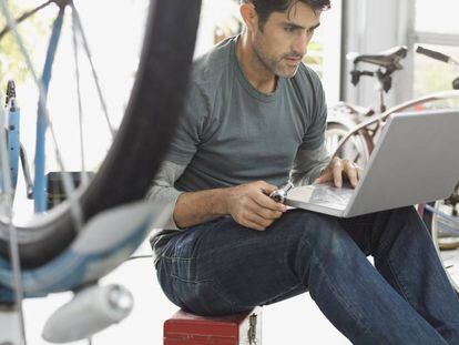 Hombre usando una computadora port&aacute;til en la tienda de bicicletas