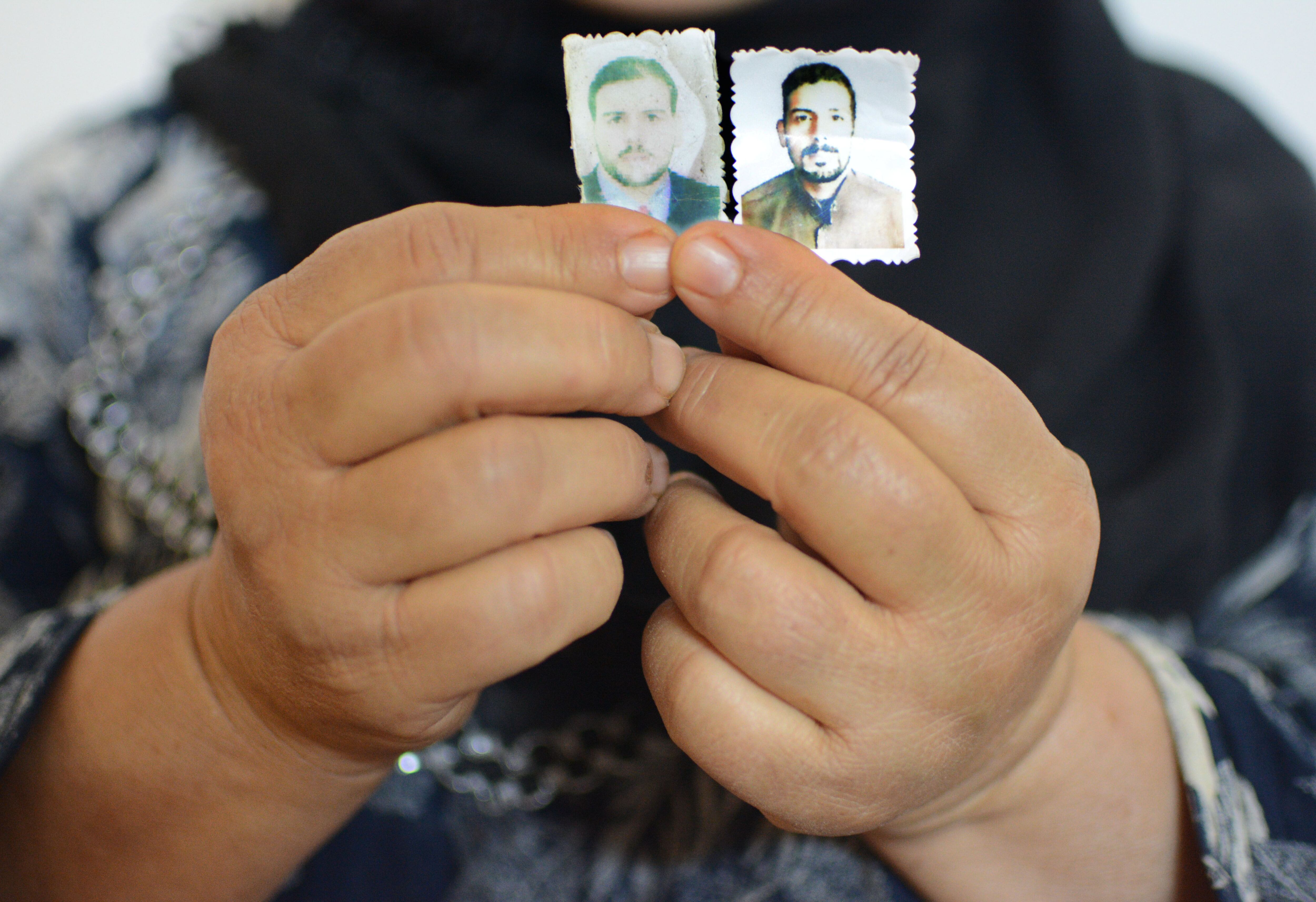 Las manos de Hadia Halil sosteniendo las fotos que conserva de sus dos hijos desaparecidos en 2016, Qahtan de entonces 37 años y Mohamed, de 31. Pincha en la imagen para ver la fotogalería completa. 