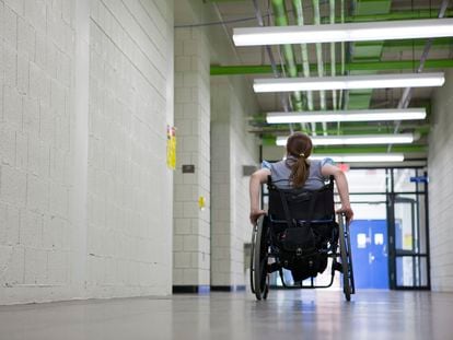 Una mujer en silla de ruedas en el pasillo de una institución educativa.