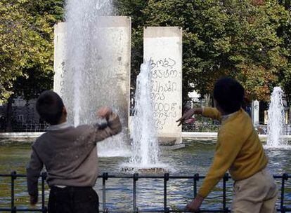 Dos niños juegan junto al estanque del parque de Berlín, frente a los tres bloques del Muro.