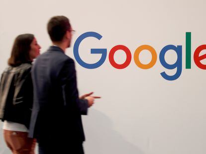 Dos personas pasan ante el logotipo de Google en un encuentro de empresas tecnológicas en París.