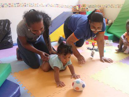Una madre juega con su hija pequeña ante la mirada de la mayor y con la ayuda de una experta, en un centro de atención a la primera infancia en Boca Chica.