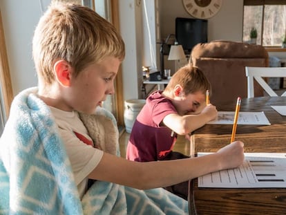 Dos niños estudian en el salón de su casa.