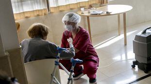 Una trabajadora protegida con un equipo contra los virus atiende a una mujer en la residencia Monte Carmelo, en Madrid.