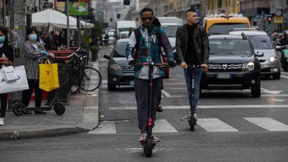 Dos hombres montan en patinete eléctrico en un carril bici emergente en Milán, Italia.
