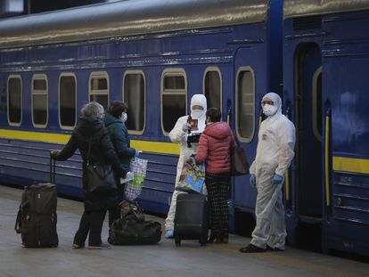 Trabajadores con trajes de protección chequean los documentos de los pasajeros en la estación de Kiev a punto de subir a un tren hacia Moscú.