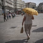 Este miércoles, una mujer cruza la Puerta del Sol central protegida por un paraguas.