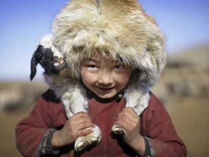 Un niño nómada lleva una oveja sobre los hombros.