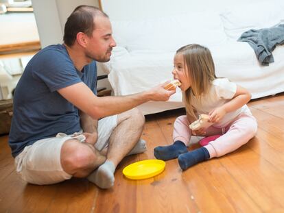 Un padre comparte un sandwich de jamón y queso con su hija.