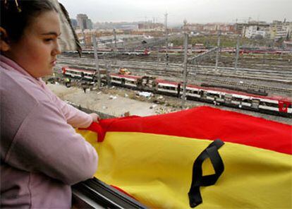 Una joven cuelga una bandera de España en su balcón, frente al tren siniestrado en Atocha.