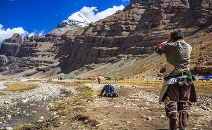 Peregrinos realizando la kora, sendero circular que rodea el sagrado monte Kailash, cuya nevada cima asoma al fondo, en el Tíbet (China).
