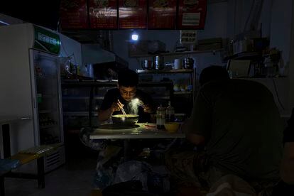Un hombre utiliza la luz de su móvil para ver mientras desayuna durante un apagón en la ciudad de Shenyang, en el noreste de China, este miércoles.