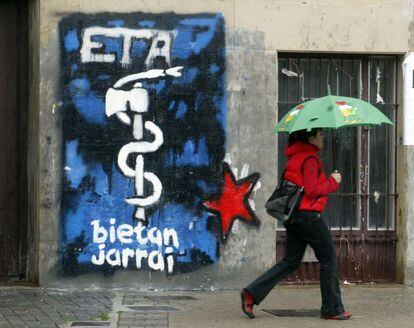 Una joven pasa junto a una pintada del anagrama de ETA en una calle de Alsasua.