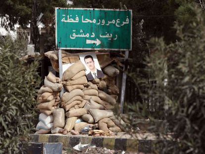 Una foto del presidente sirio Bachar el Asad cuelga de un muro de sacos colocados por el Ej&eacute;rcito cerca de la ciudad de Harasta, nueve kil&oacute;metros al norte de Damasco.