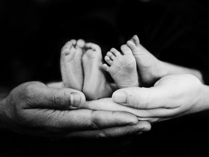Dos padres sujetan los pies de sus bebés mellizos.