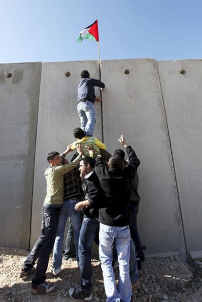 Jóvenes palestinos colocan su bandera en el muro erigido por Israel.