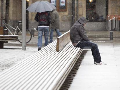Un hombre aguanta la nieve sentado en un banco del centro de Vitoria, que sufre hoy la cuarta nevada de este año.