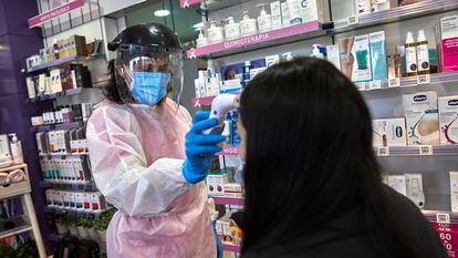 Una farmacéutica toma la temperatura a una mujer antes de realizarle un test de antígenos en una farmacia de Madrid (España), en febrero.