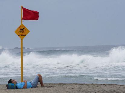 Un turista descansa bajo la bandera roja de alerta ante la cercanía del huracán Agatha a las costas de Puerto Escondido, Oaxaca.