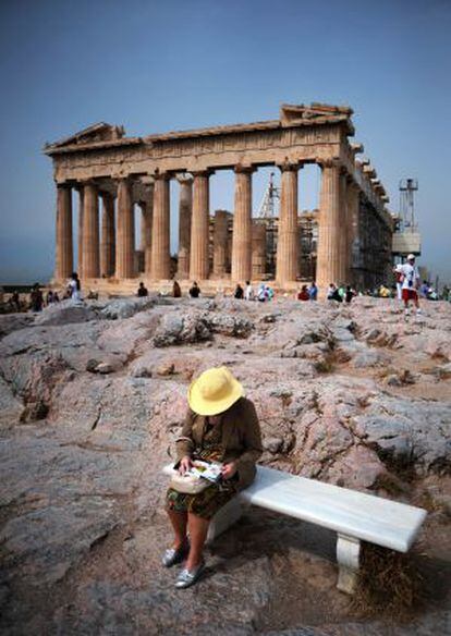 Una turista consulta su guía de viaje sentada junto al Partenón, en la Acrópolis de Atenas.