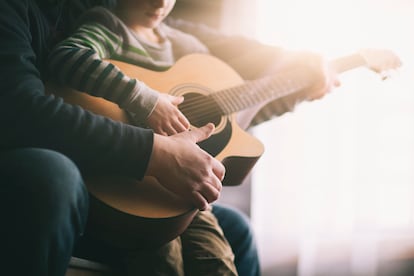 father teaching son to play guitar