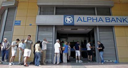 Varias personas hacen cola para sacar dinero en efectivo en un par de cajeros de Atenas