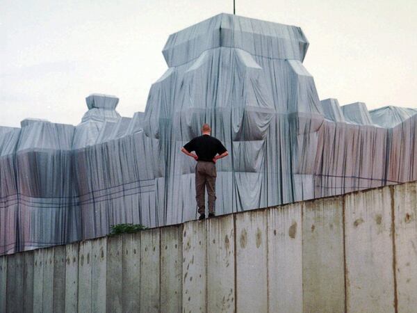Un hombre sobre el Muro de Berlín contempla la obra de Christo sobre el edificio Reichstag, en junio de 1995.