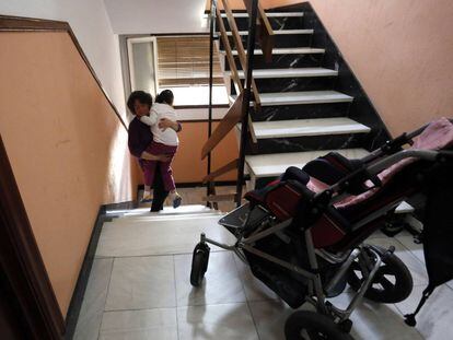 Una mujer sube en brazos a su hija con discapacidad a su casa en Madrid.