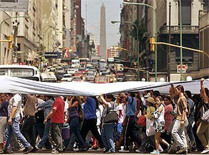 Cientos de parados recorren en una manifestación el centro de Buenos Aires bajo una inmensa bandera argentina.