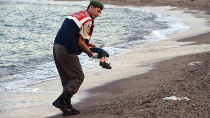 Un policía recoge el cadaver de un niño en una playa de Turquía.