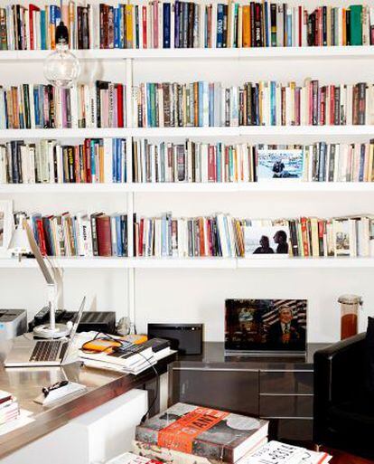 El despacho de Varoufakis en su casa. Además de su ordenador y un volumen sobre Warhol, en su librería se encuentra una foto junto a su esposa y una pieza de arte satírico con una ilustración de George W. Bush y la leyenda: “El mayor fracaso de América”.