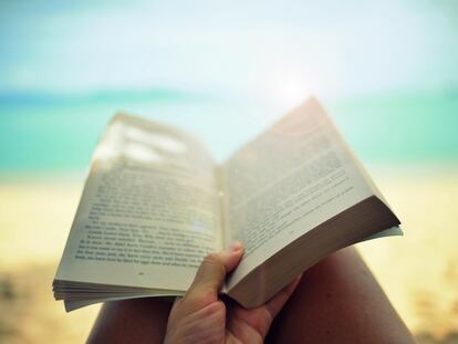 Una persona lee un libro en la playa.