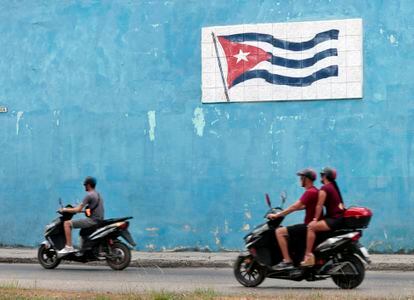 Motociclistas cruzan frente a un mural con la bandera cubana este miércoles en La Habana.
