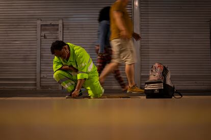 Two passersby walk at dawn while Felix removes gum from the ground.