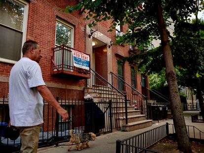 Un hombre pasea a su perro en el East Village de Nueva York junto a un cartel de se alquila piso.