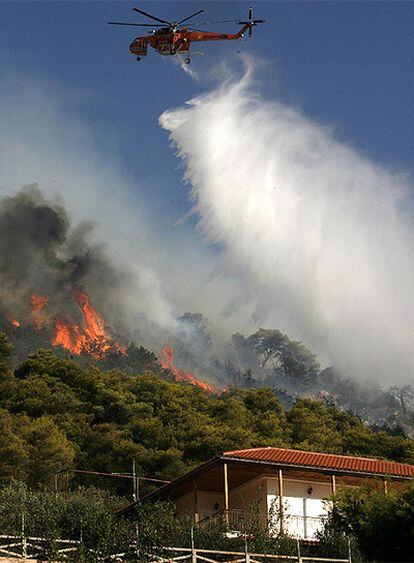 Un helicóptero lanza agua sobre las llamas que rodean una casa en Anatoli, al noreste de Atenas
