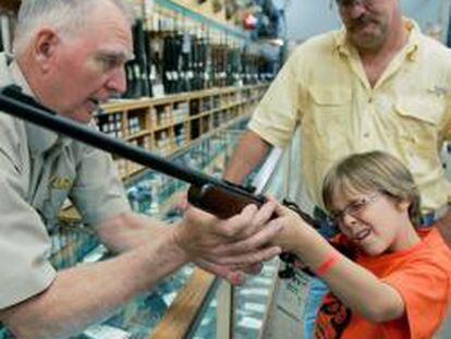 Un distribuidor de armas ayuda a un niño a sujetar un rifle en presencia de su padre en Fort Worth, Texas.