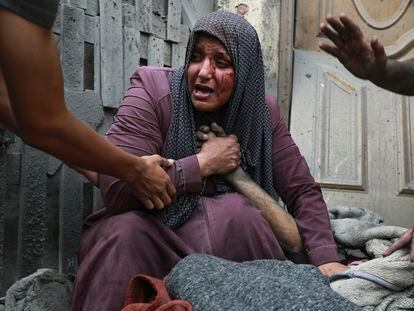 Una mujer palestina herida llora mientras sostiene la mano de su familiar muerto frente a su casa, tras los ataques aéreos israelíes dirigidos contra su barrio en la ciudad de Gaza, este lunes.