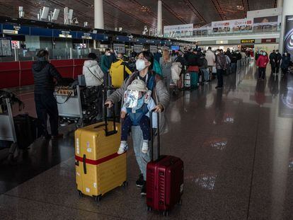 Una mujer lleva a su bebé mientras empuja dos maletas en el aeropuerto de Pekín.