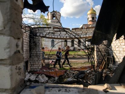 Tres niños juegan frente a una iglesia dañada durante la invasión rusa de Ucrania, en el pueblo de Kolychivka.