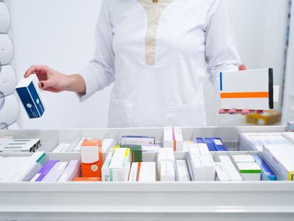 Una farmacéutica coge medicamentos de un estante de una botica.