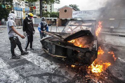 Tres manifestantes permanecen junto a un coche en llamas durante la jornada de paro nacional convocada por la oposición, en Caracas.