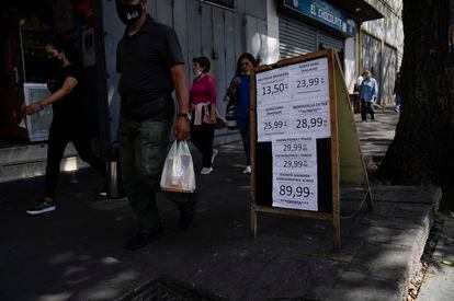 Los peatones pasan frente a un cartel que muestra los precios del producto en bolívares, en Caracas, Venezuela.
