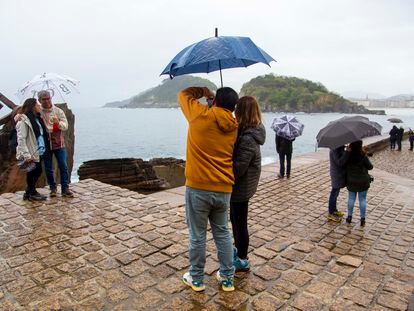 Varios turistas con paraguas visitan el Peine del Viento, en San Sebastián, este domingo.