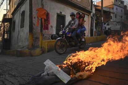 Dos personas con máscara protectora pasan en una motocicleta cerca de una efigie en llamas que representa a Judas Iscariote durante la Semana Santa en el barrio de Catia, uno de los barrios marginales y más pobres de Caracas (Venezuela).